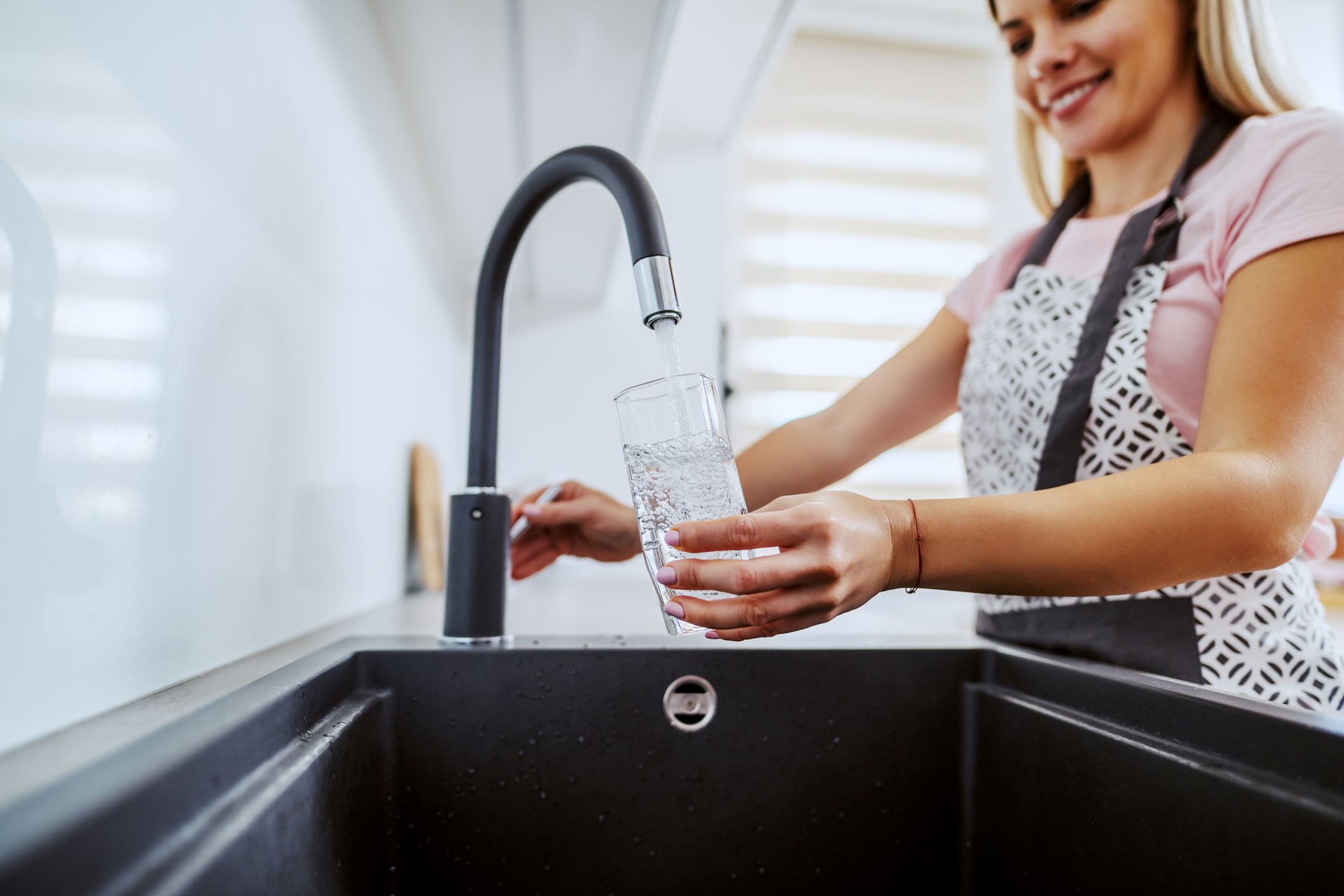 A woman fills a water glass at a sink.